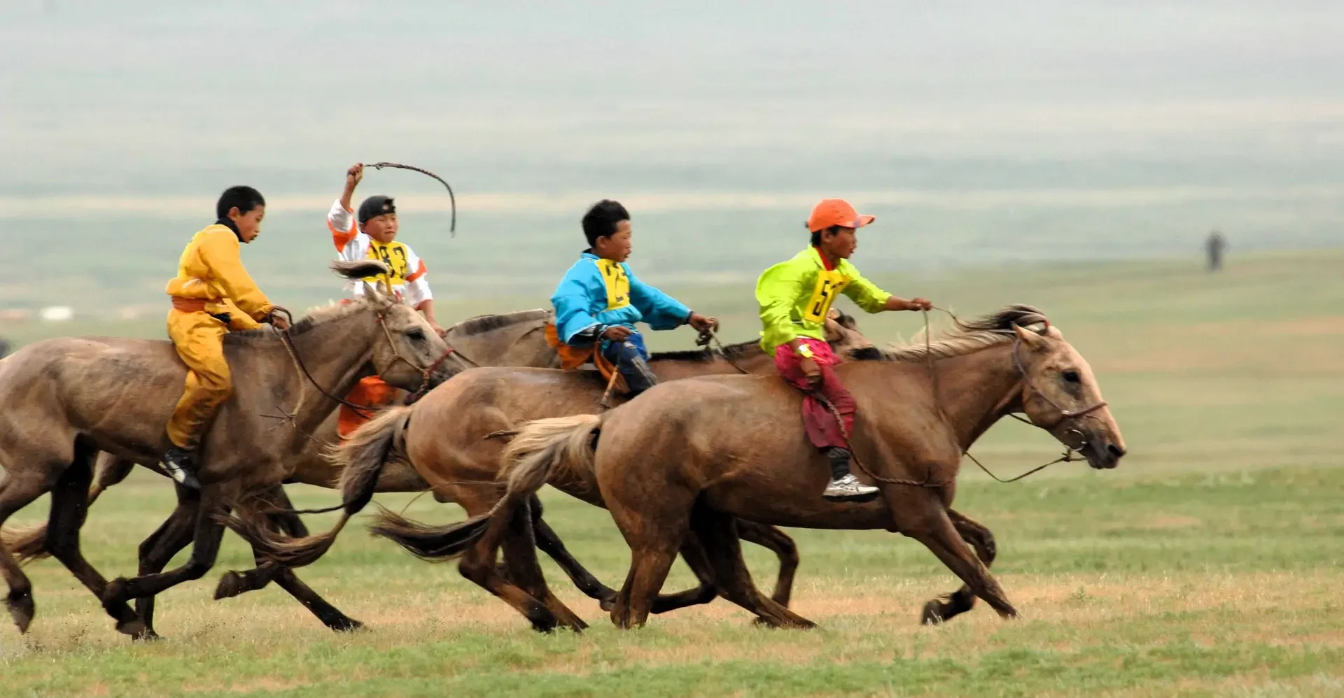 "Four children riding horses at full gallop during a traditional horse racing event at the Naadam Festival in Mongolia."