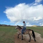 Horse rider crossing open steppe under vivid rainbow — Mongolia Horseback Riding Steppe Trek
