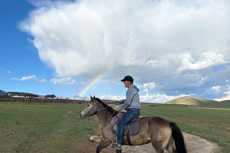 Horse rider crossing open steppe under vivid rainbow — Mongolia Horseback Riding Steppe Trek
