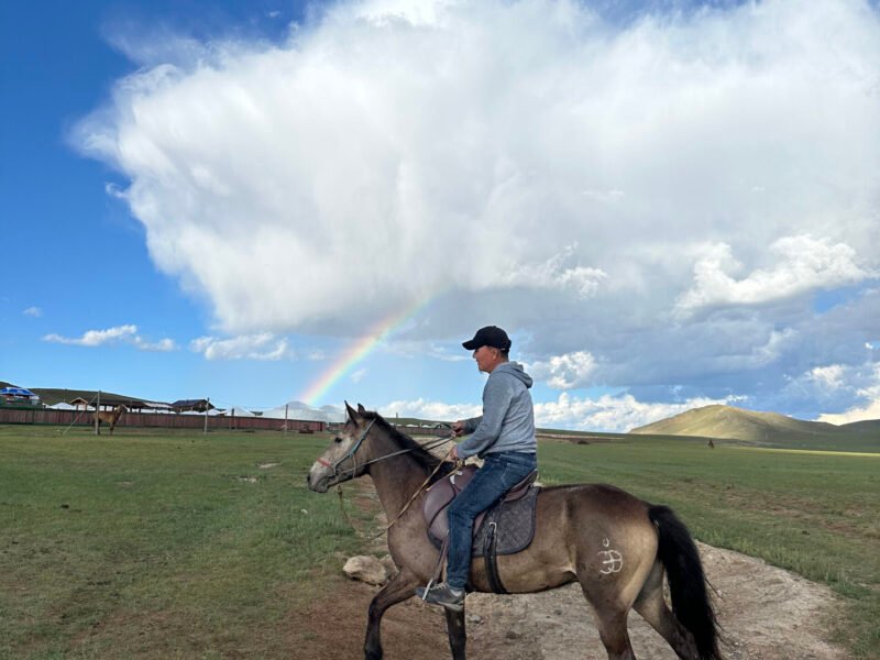 Horse rider crossing open steppe under vivid rainbow — Mongolia Horseback Riding Steppe Trek