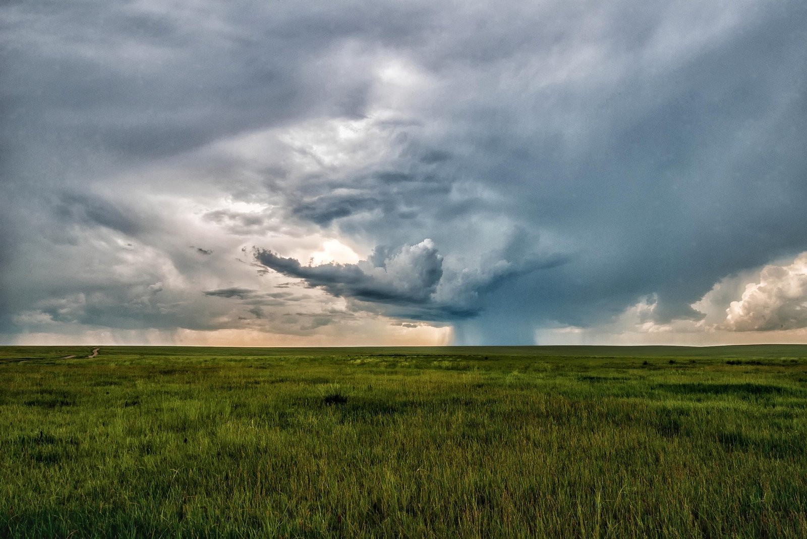Empty dirt road winding across flat Mongolian steppe with storm clouds building on the horizon