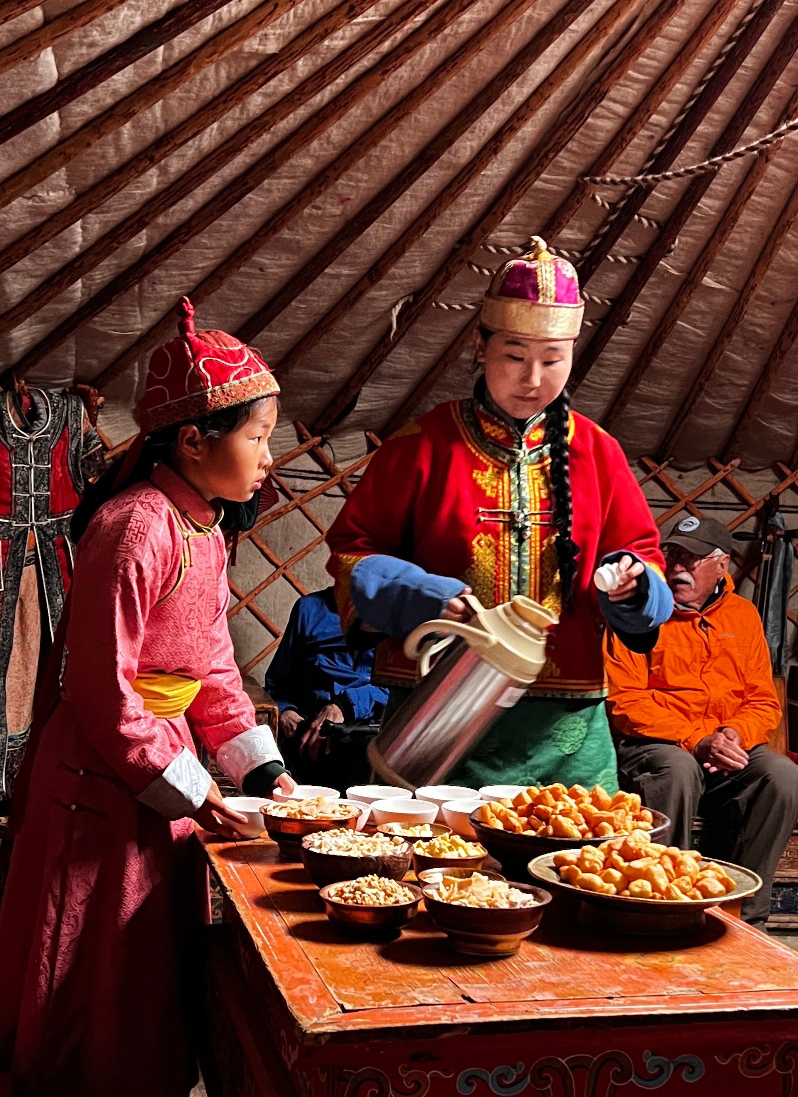Mongolian woman and child in traditional dress serving dairy products and boortsog inside a ger