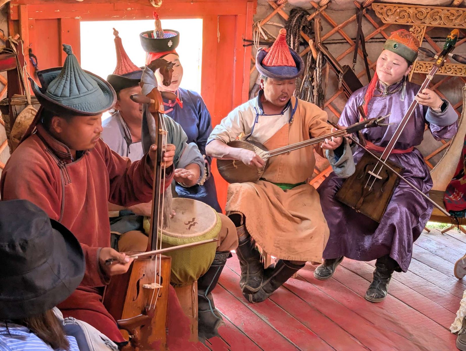 Mongolian musicians in traditional dress playing morin khuur instruments inside a ger during a cultural gathering