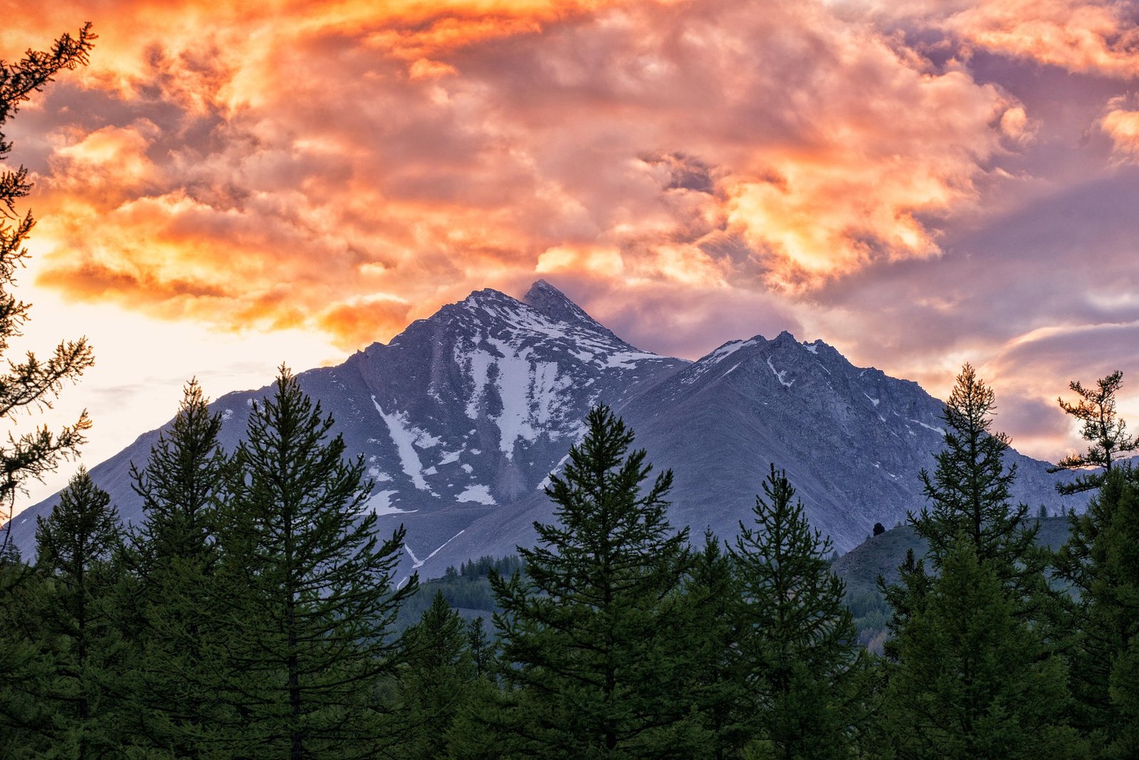 Snow-capped Altai Mountain peak silhouetted against a fiery red and orange sunset sky in western Mongolia