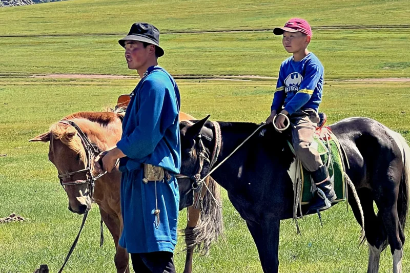 Local guide and young rider with two horses on Mongolia's green grassland steppe
