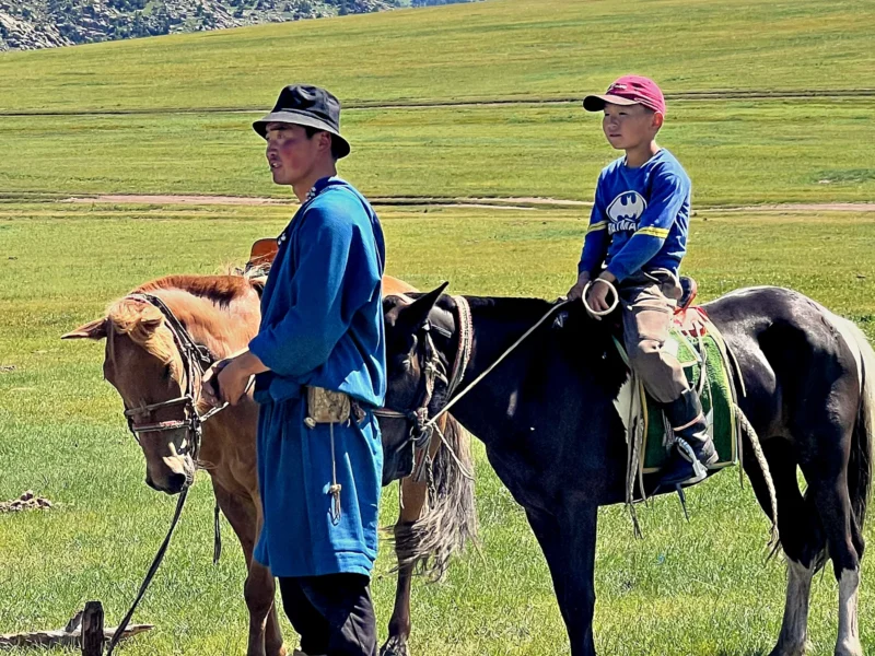 Local guide and young rider with two horses on Mongolia's green grassland steppe