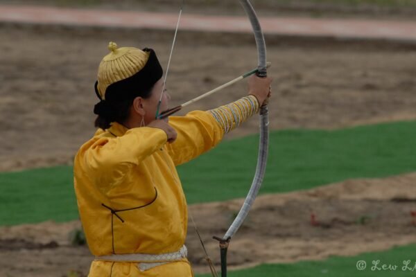 A Mongolian archer in a yellow deel draws a bow at Naadam
