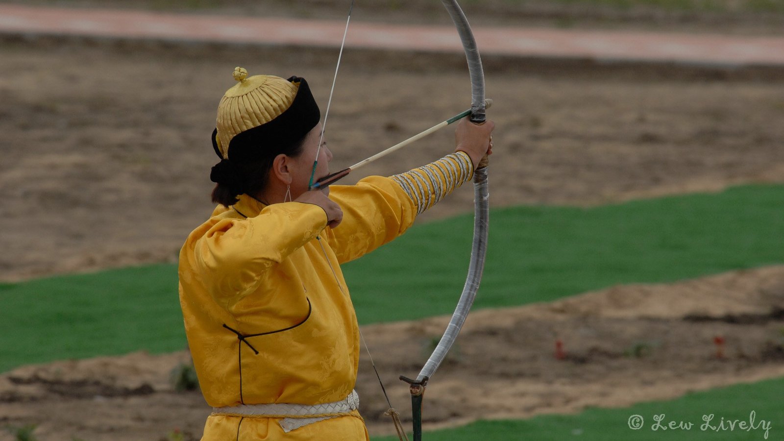 A Mongolian archer in a yellow deel draws a bow at Naadam