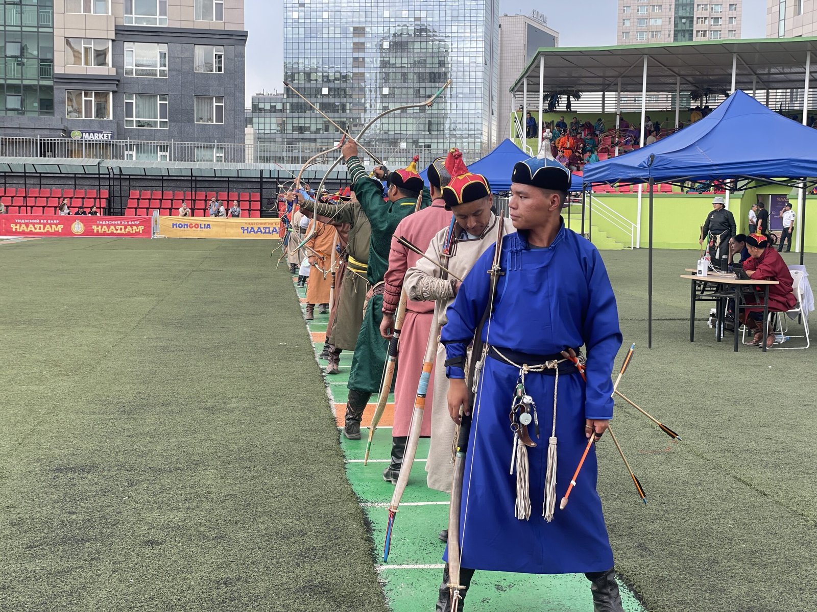 A line of Mongolian archers in traditional deel taking aim at Naadam
